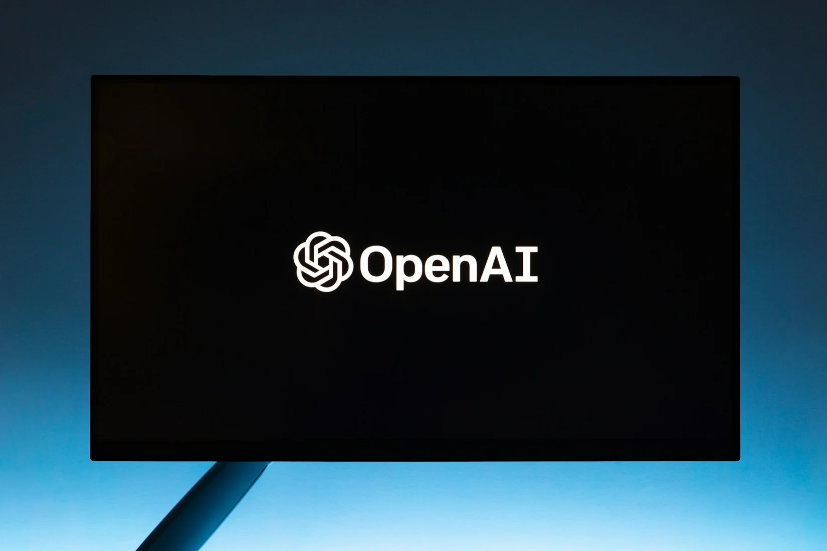파란 조명 아래 모니터에 표시된 OpenAI 로고를 촬영한 실제 사진.